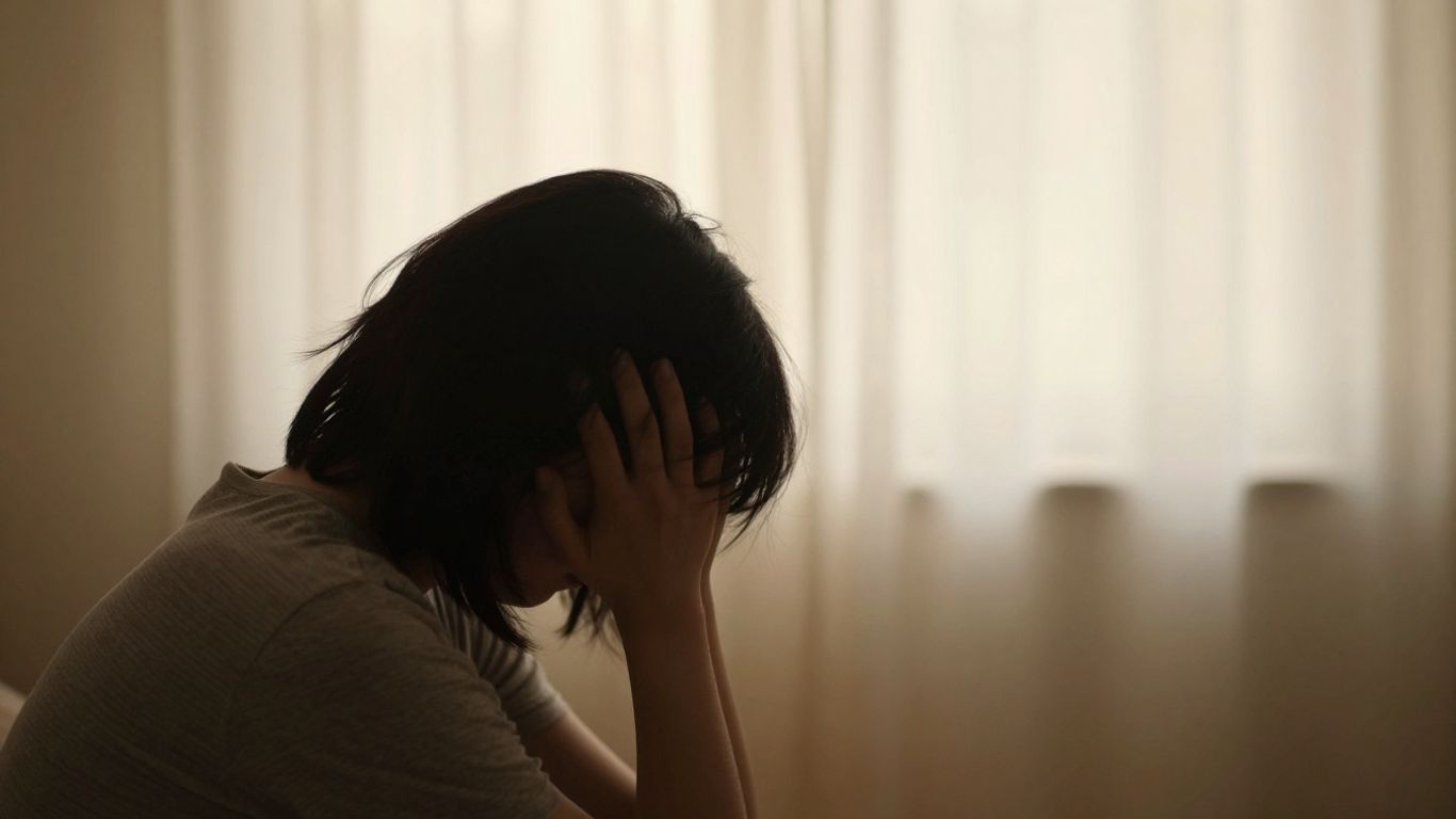 Person contemplating, head in hands, soft background.