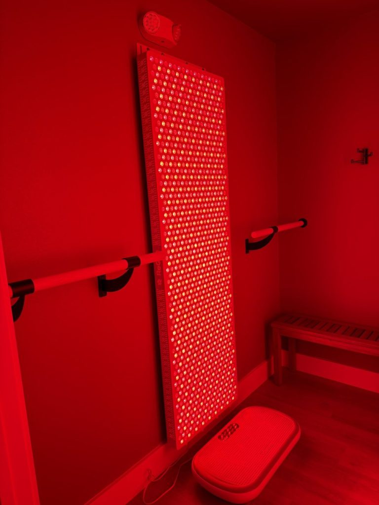 Red light therapy panel with a vibration plate on the floor at Adoration